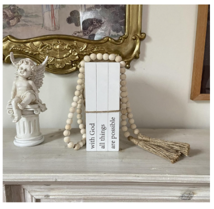 Decorative white faux books with "With God All Things Are Possible" quote, accompanied by a farmhouse bead garland with tassels.